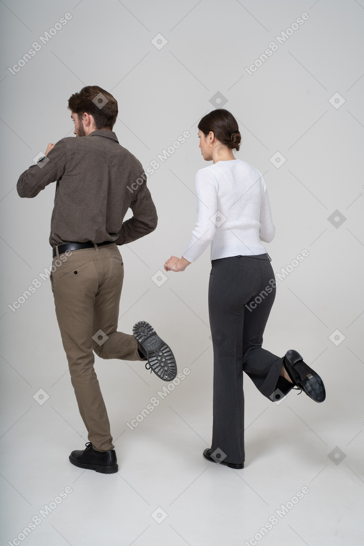 Vue de trois quarts arrière d'un jeune couple en tenue de bureau levant la jambe