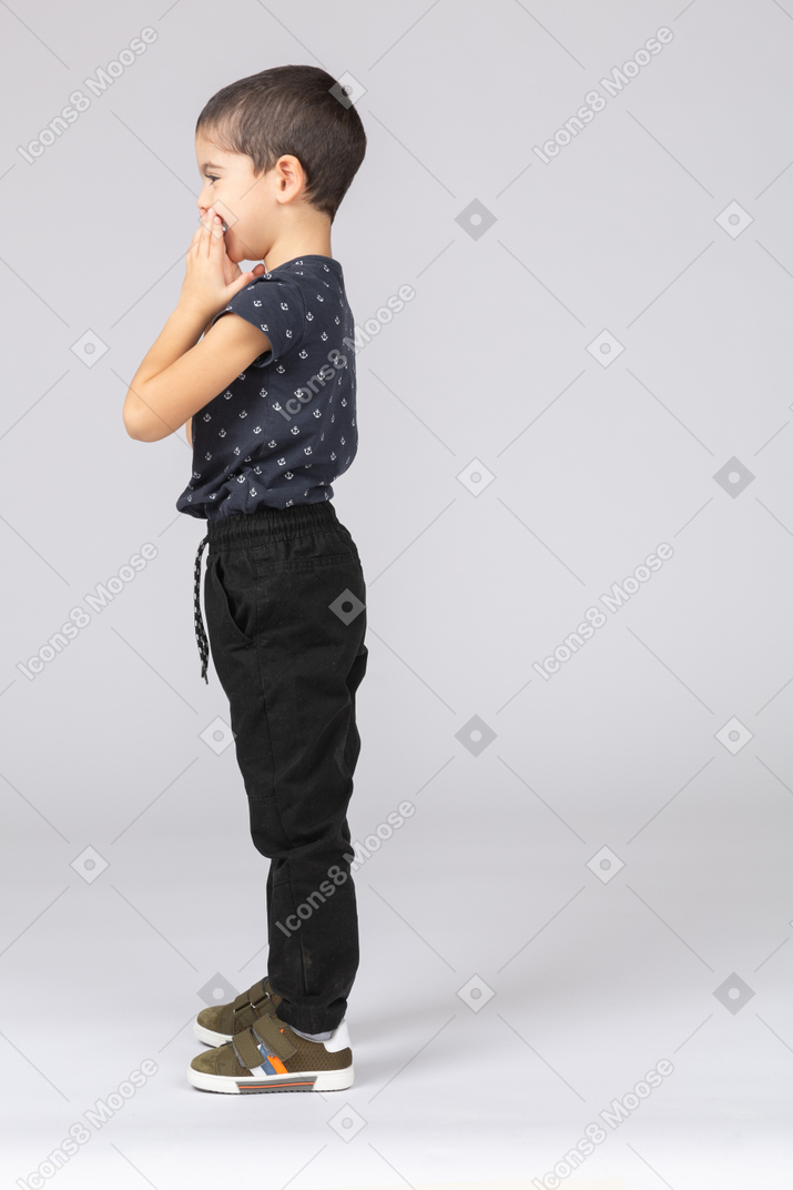 Side view of cute boy covering mouth with hands