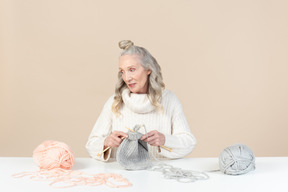 Femme âgée concentrée sur le tricot et regardant de côté