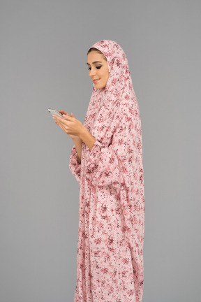 Улыбается арабская женщина, используя свой мобильный телефон