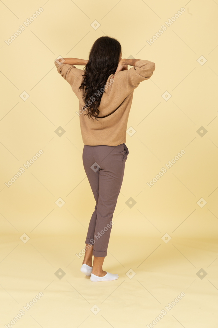 Vista traseira a três quartos de uma jovem fêmea de pele escura tocando seus ombros