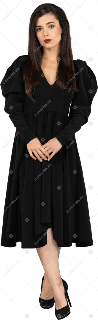 Vista frontale di una giovane donna in un abito nero che tengono le mani insieme