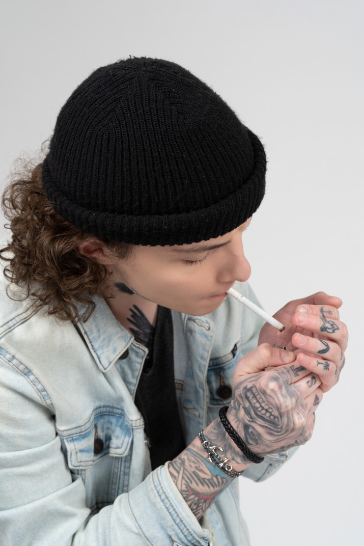 Young man with tattooed hands lighting a cigarette