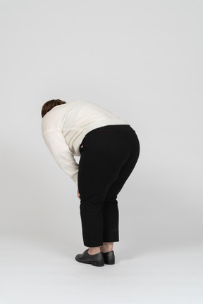 Rear view of a plump woman in white sweater bending down