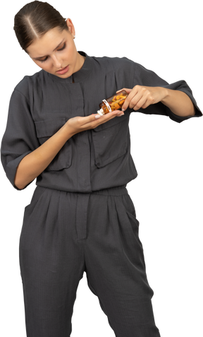 Front view of a young woman in a jumpsuit pouring the pills out of a jar