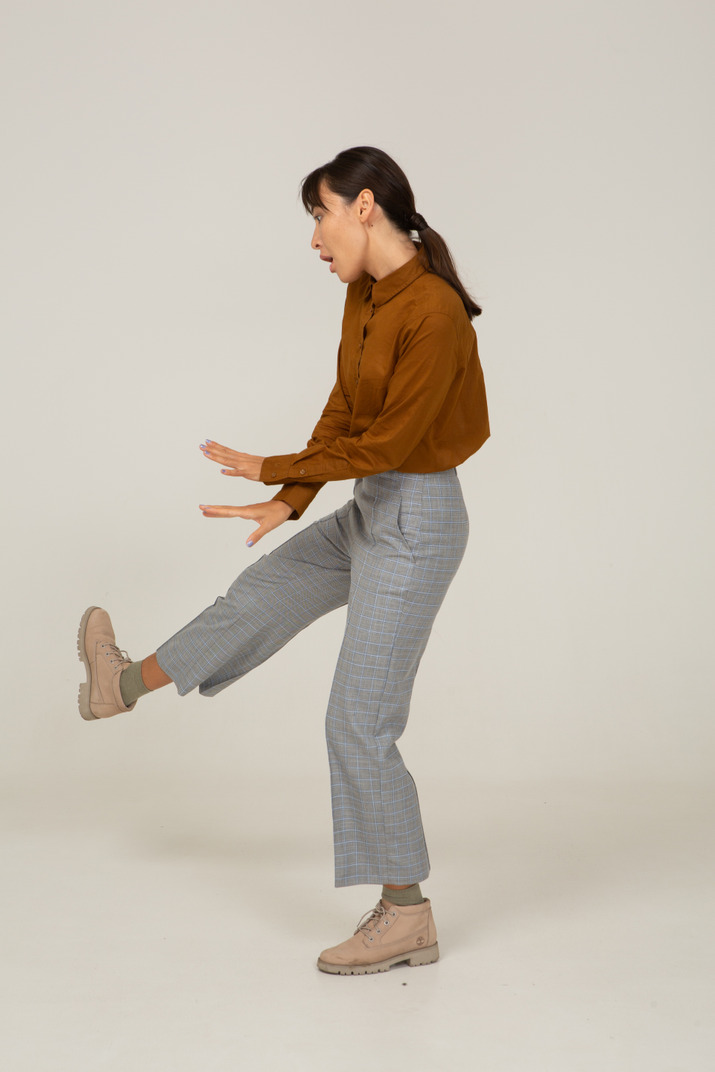 Side view of a dancing young asian female in breeches and blouse raising leg