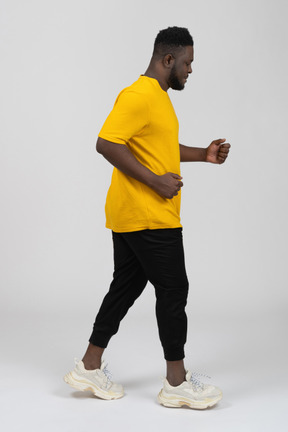 Vista lateral de un joven hombre de piel oscura que camina en camiseta amarilla