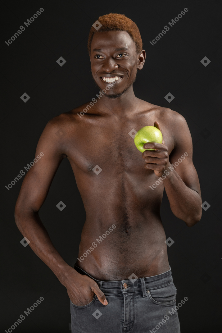Крупным планом молодой человек, уверенно стоящий и улыбающийся, держит яблоко