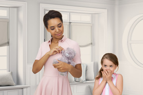 Young woman holding teddy bear and little girl covering her mouth with hands