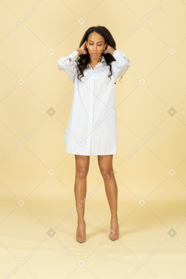 Vista frontale di una giovane donna dalla carnagione scura in abito bianco, che fissa i suoi capelli