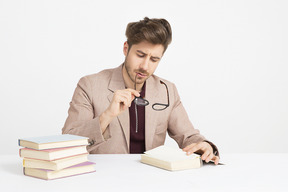 Beau jeune homme tenant ses lunettes et lire un livre