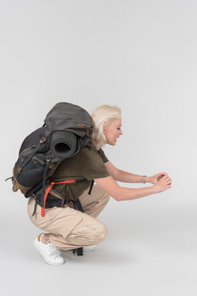 Mature female tourist carrying heavy backpack and making photos with smartphone