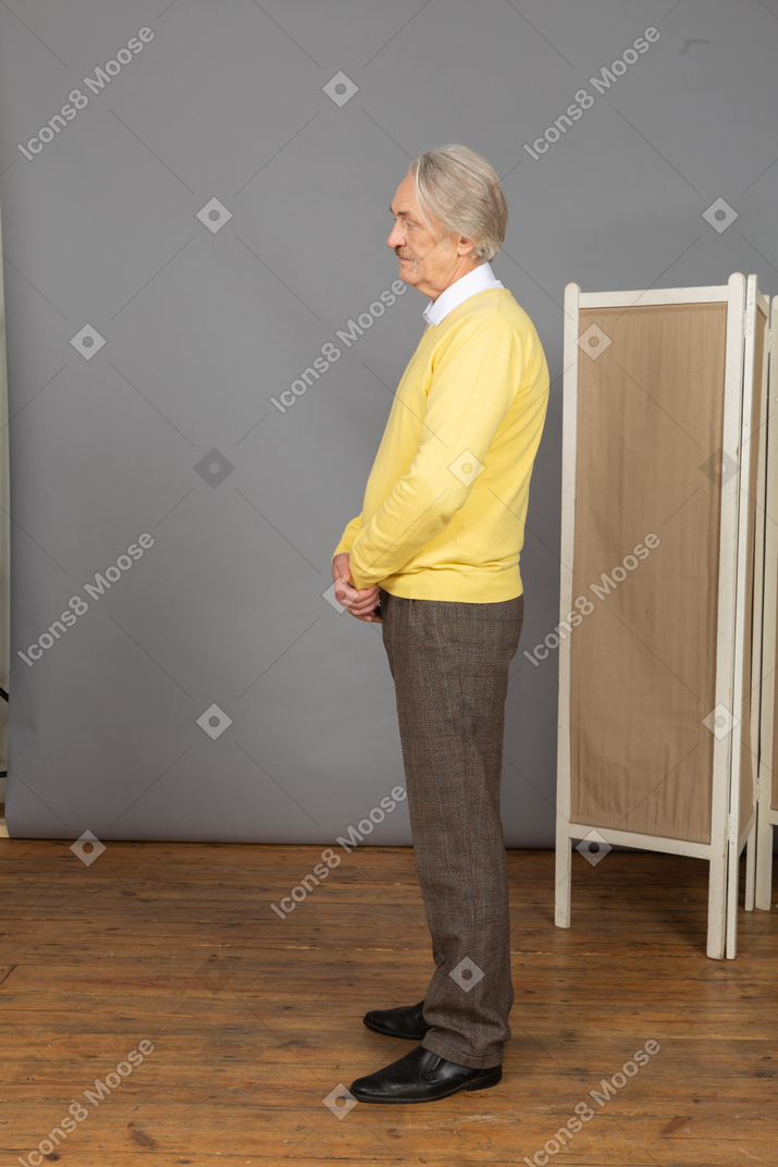 Side view of an old man holding hands together while standing still