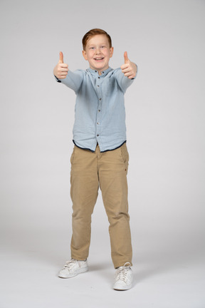 Vista frontal de um menino feliz, mostrando os polegares e olhando para a câmera