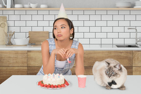 A woman sitting at a table with a cake and a cat