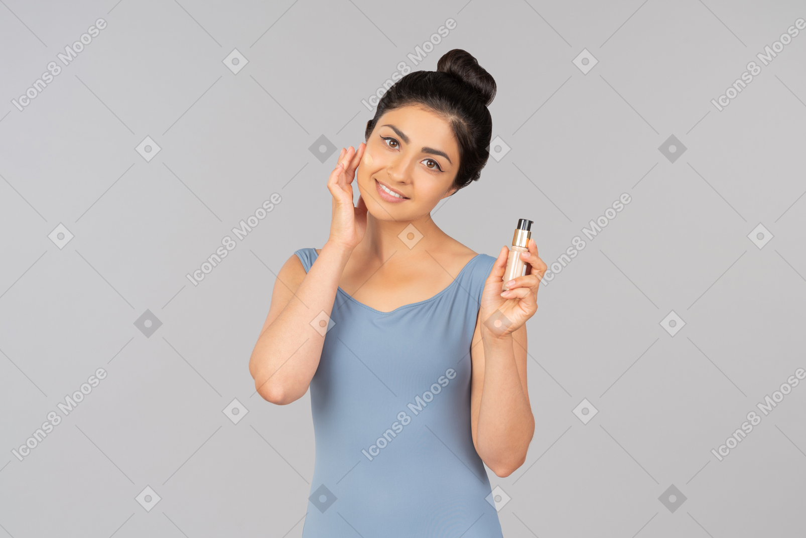 Giovane donna indiana con fondotinta tonale sul viso tenendo una bottiglia di fondotinta tonale