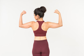 Young indian woman in sportswear showing muscles and standing back to camera