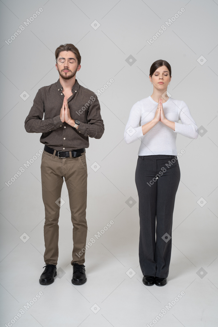 Vista frontale di una giovane coppia in preghiera in abiti da ufficio che si tiene per mano insieme