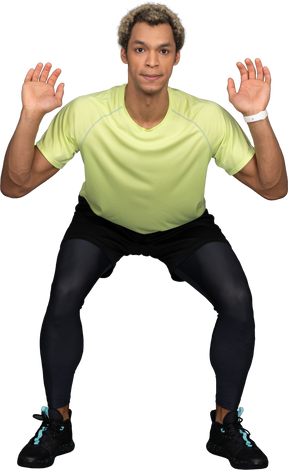Front view of a squatting dark-skinned young man raising hands
