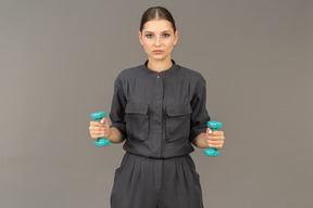 Front view of young woman in a jumpsuit doing exercises with dumbbells