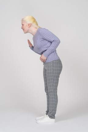 Vista lateral de una joven agachándose y gimiendo con mal estómago