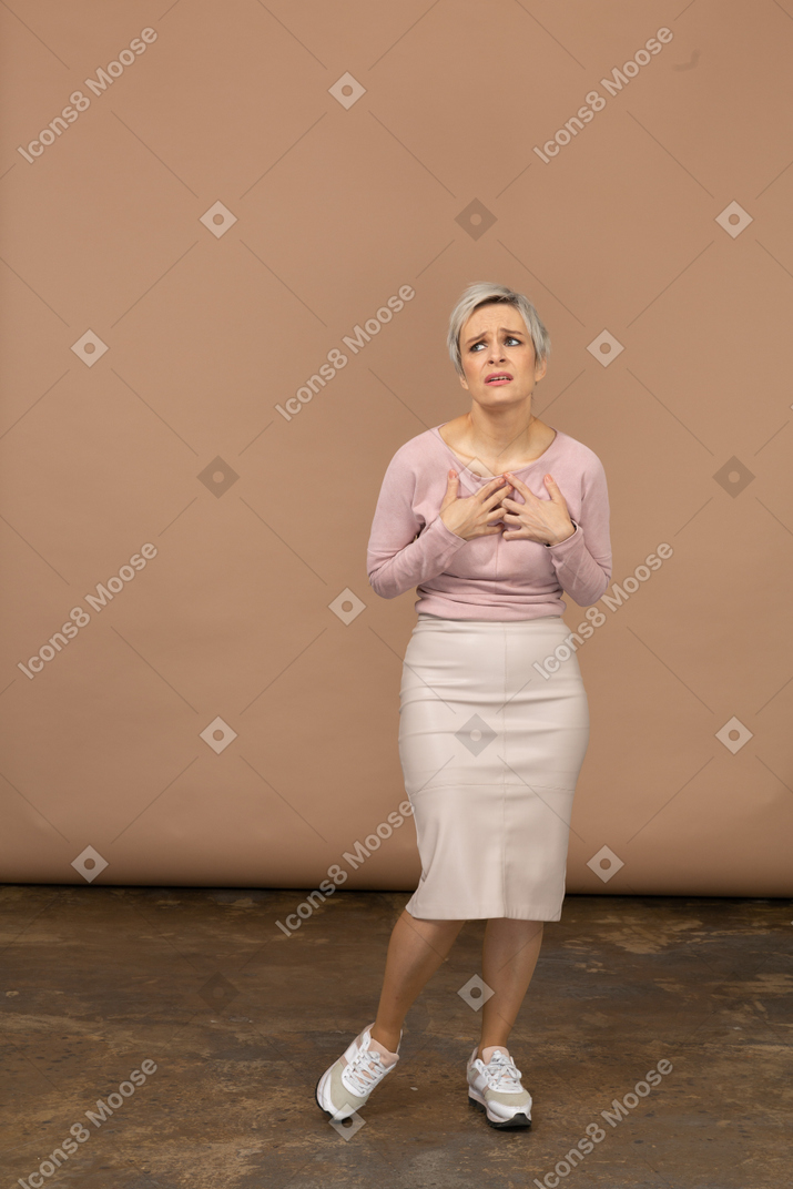 Front view of an emotional woman in casual clothes standing with hands on chest and looking up