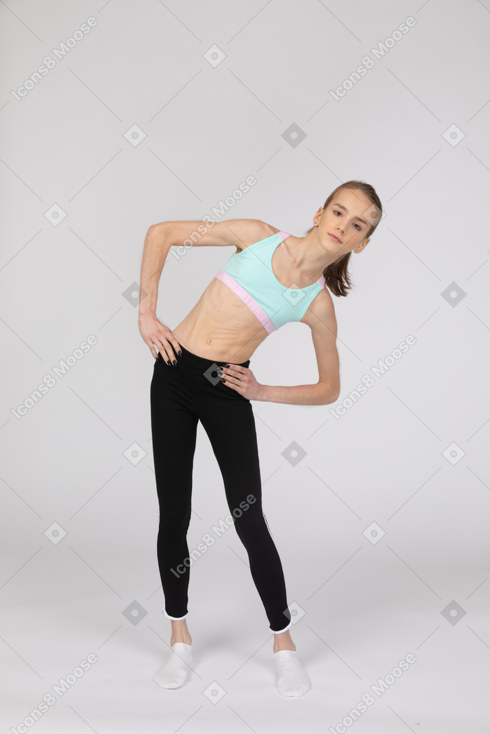 Side view of a teen girl in sportswear squatting and putting hands on hips