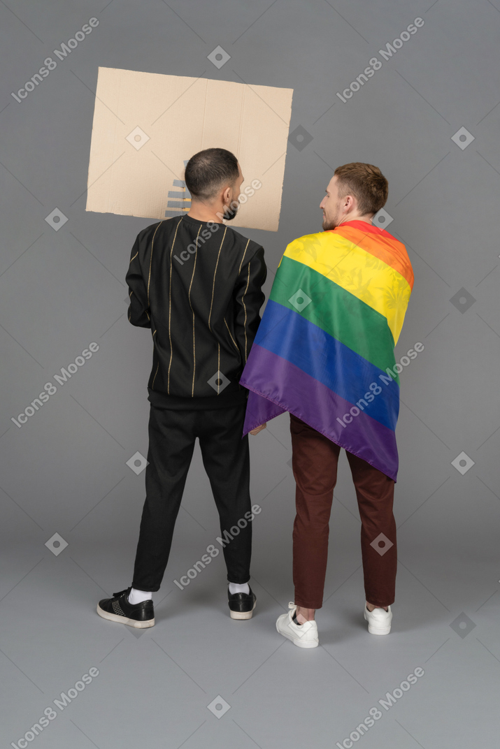 Back view of two young men with a billboard and lgbt flag