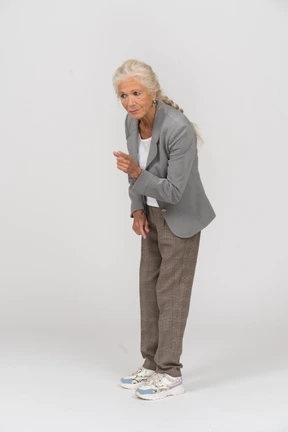 Side view of an old lady in suit bending down and showing warning sign