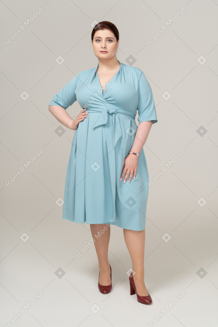 Вид спереди женщины в синем платье позирует с рукой на бедре