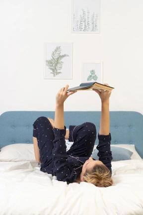 Full-length of a bored young lady trying to read book in bed