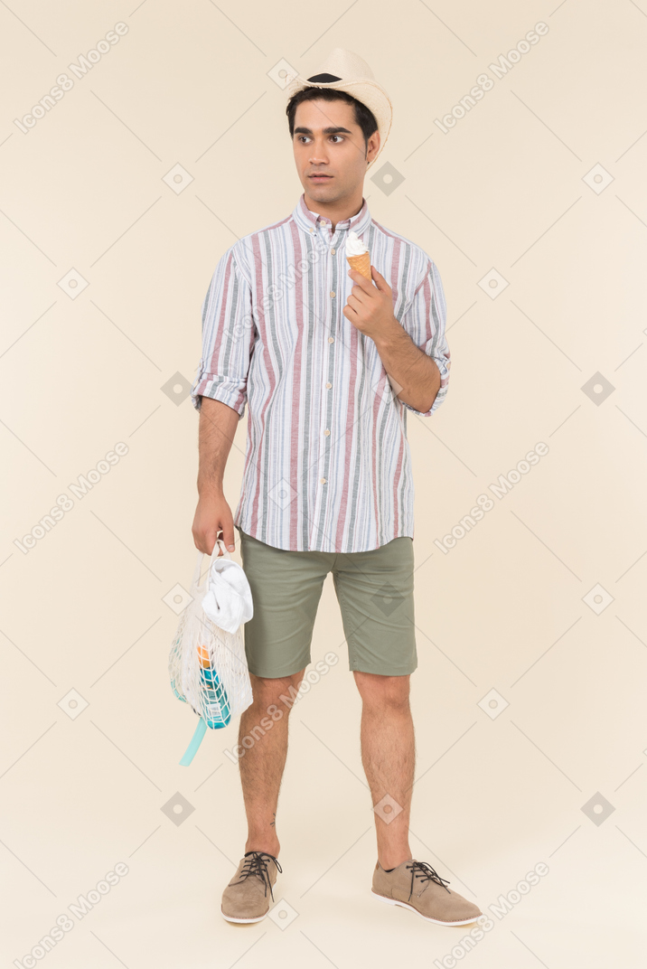 Слегка удивленный молодой человек держит авоску и мороженое