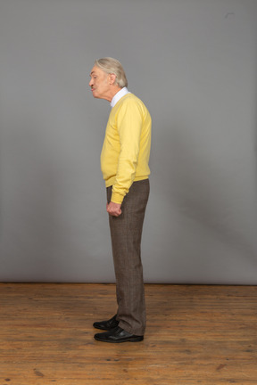 Side view of an old man in a yellow pullover bending down and showing tongue