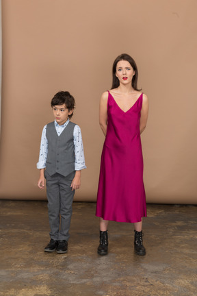 男の子が彼女の近くに立っている間、背中の後ろに腕を持っている赤いドレスの女性
