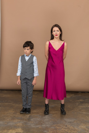 Woman in red dress holding arms behind back while boy standing near her