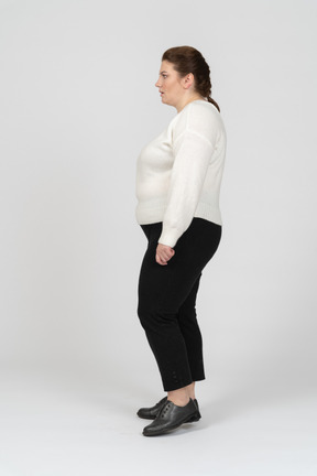 Plus size woman in white sweater standing in profile
