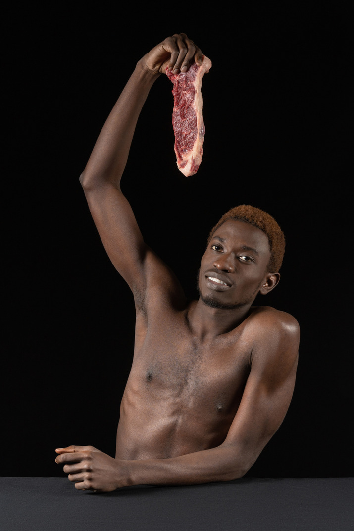 Front view of a young afro man holding a slice of meat