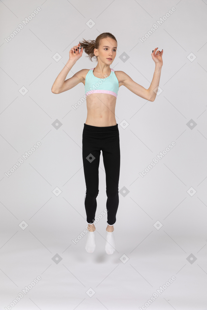 Front view of a teen girl in sportswear raising hands while jumping