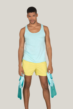 Man in blue tank top and yellow shorts holding flippers