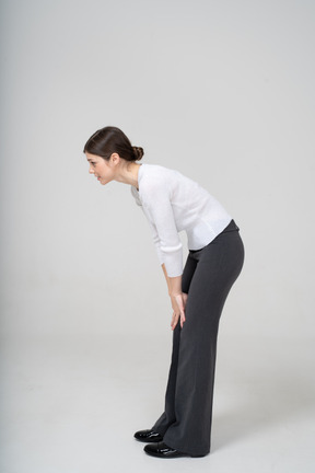 Side view of a woman in white shirt and black pants bending down