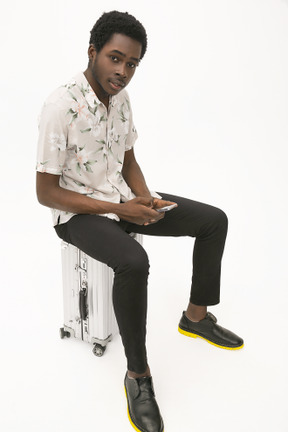 Afroman sitting on the baggage and using his smartphone