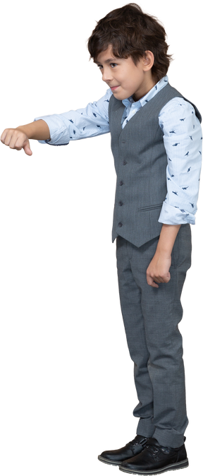 Вид сбоку на мальчика в сером костюме, показывающего большой палец вниз