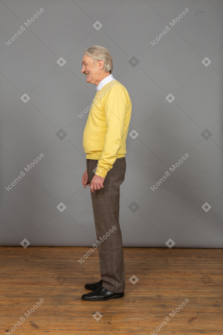 Side view of a smiling happy old man in a yellow pullover looking aside