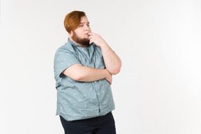 Songeur jeune homme en surpoids debout avec les mains croisées