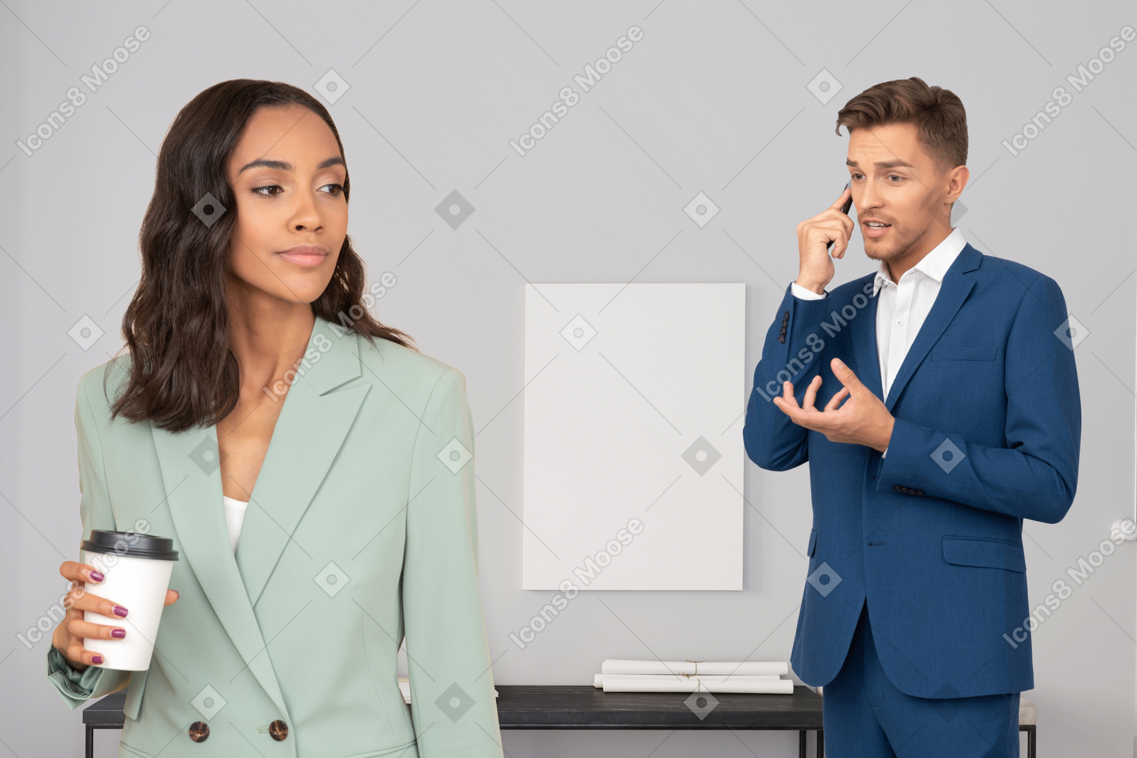 Man in suit talking on the phone while woman next to him holding cup of coffee