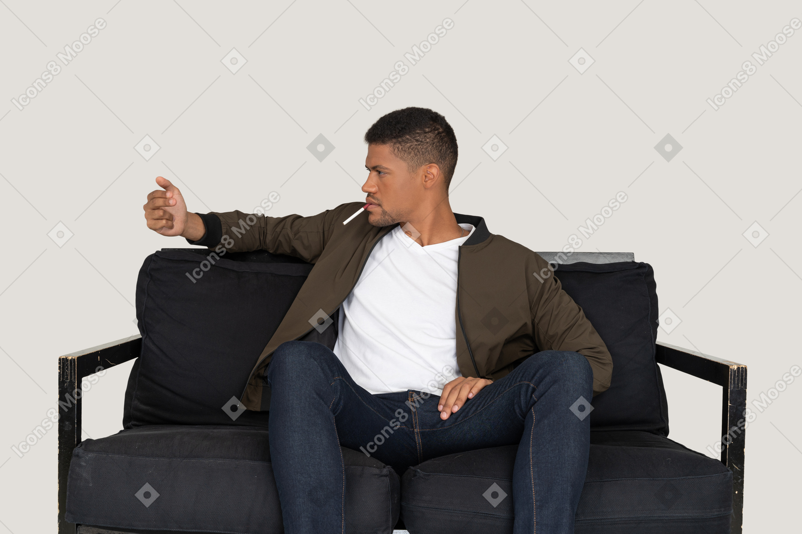 Vue de face du jeune homme assis sur un canapé et tenant une cigarette dans la bouche