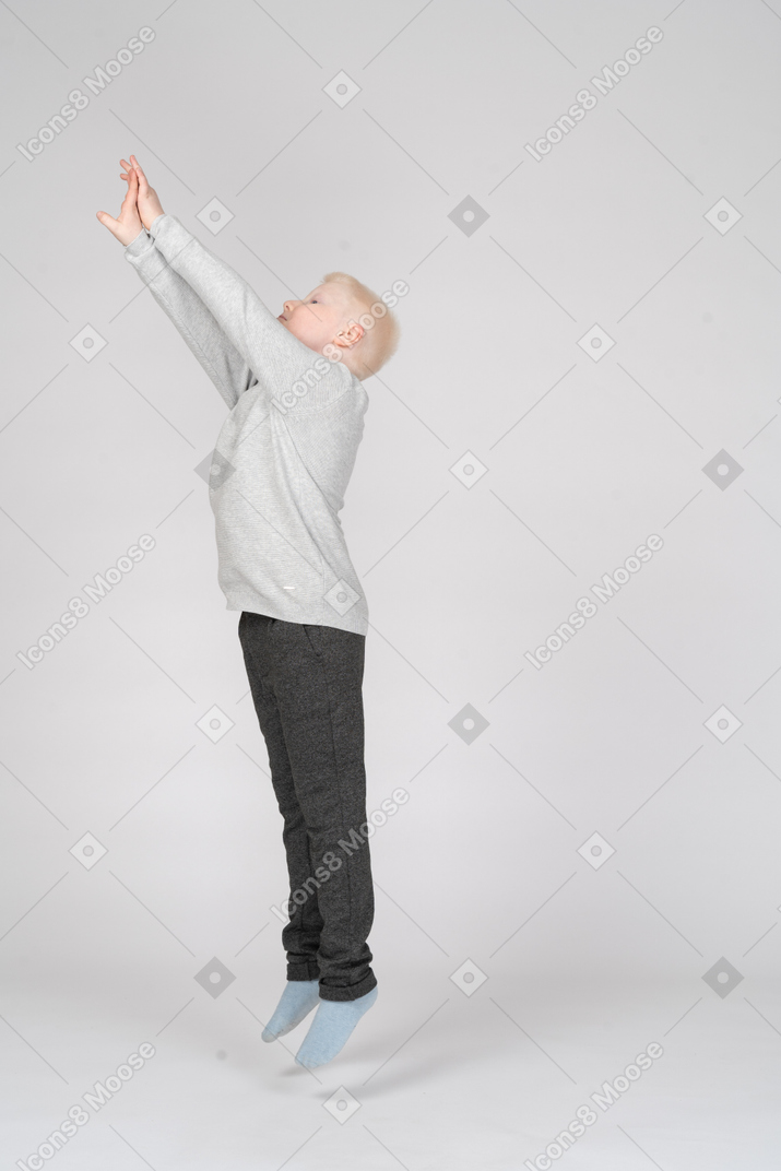 Vista lateral de um menino pulando com as mãos levantadas