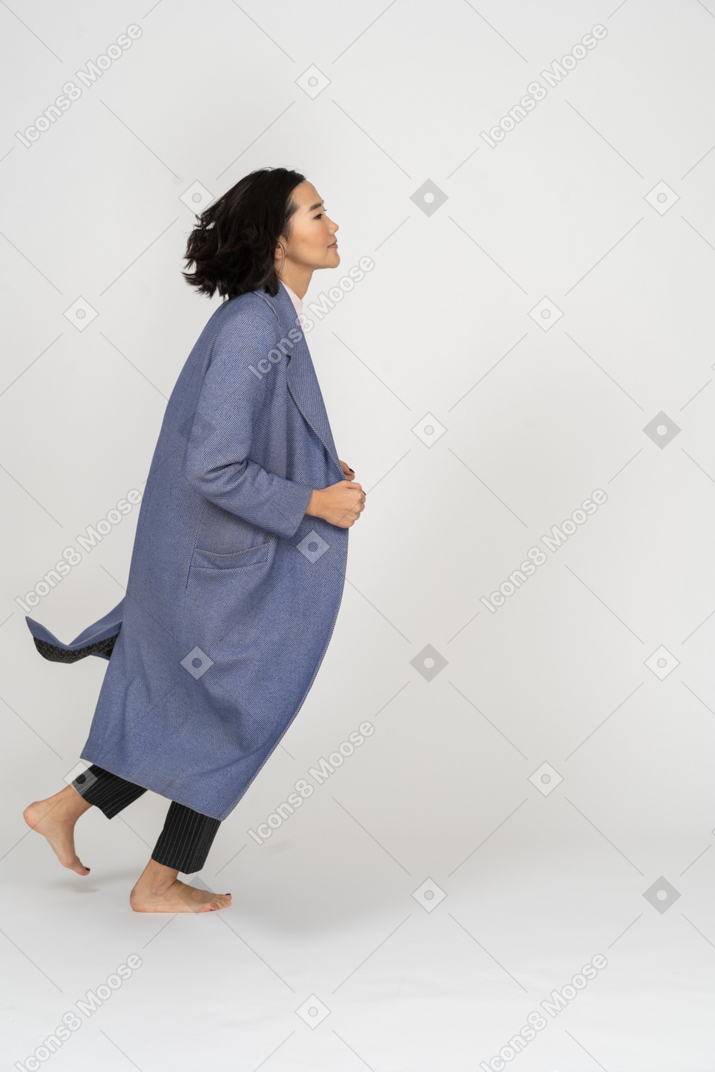 Vista laterale della donna che cammina e tiene il cappotto