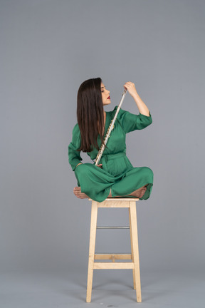木製の椅子に足を組んで座っているクラリネットを見ている若い女性の全身