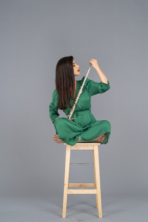 Toute la longueur d'une jeune femme regardant la clarinette assise avec ses jambes croisées sur une chaise en bois